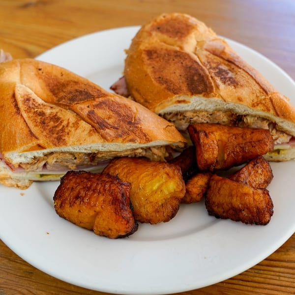 Two halves of a Cuban sandwich with roasted plantains on a white plate.