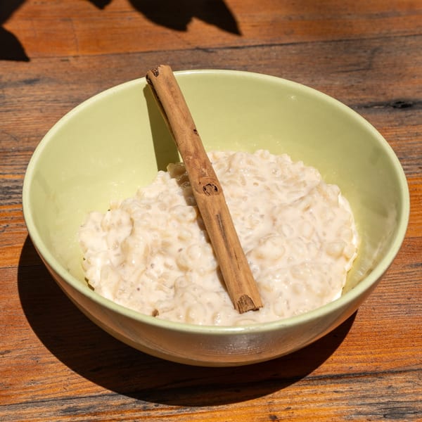 Arroz con Leche, a Cuban rice pudding with a cinnamon stick, in a light green bowl.