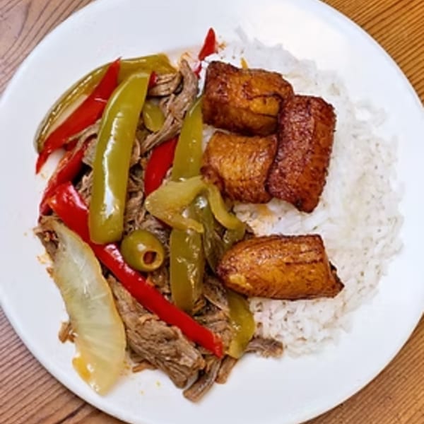 Ropa Vieja with white rice, green and red peppers, onions, an olive, and fried plantains.