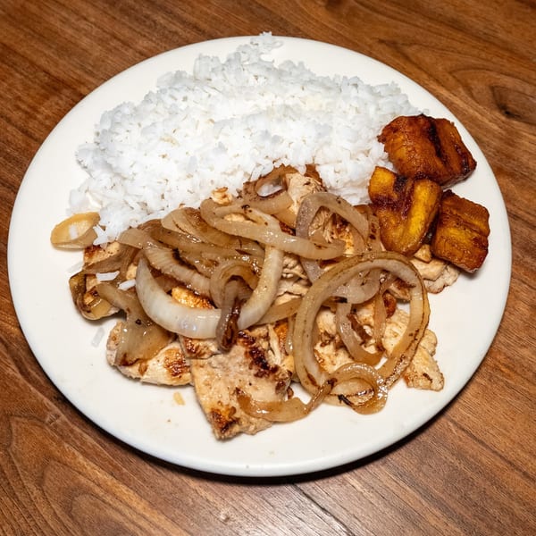Cuban-style grilled chicken with sautéed onions, white rice, and fried plantains on a white plate.
