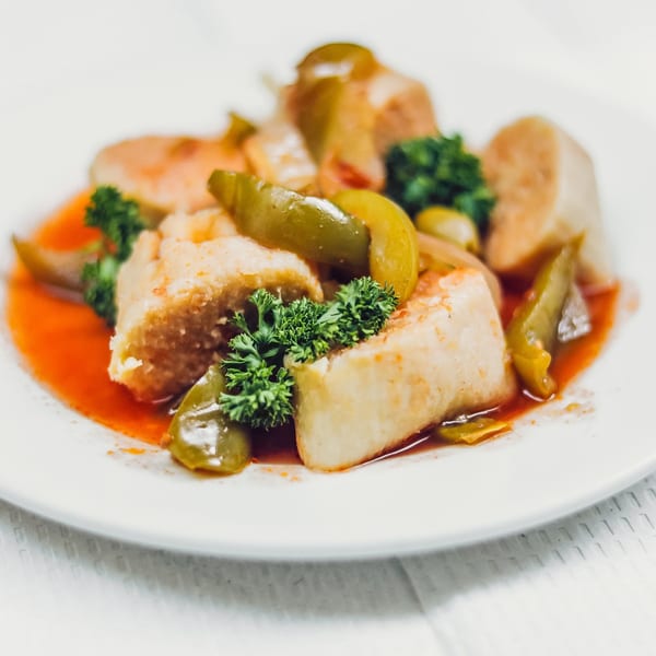 Cuban tamales with green peppers and parsley in a red sauce on a white plate.