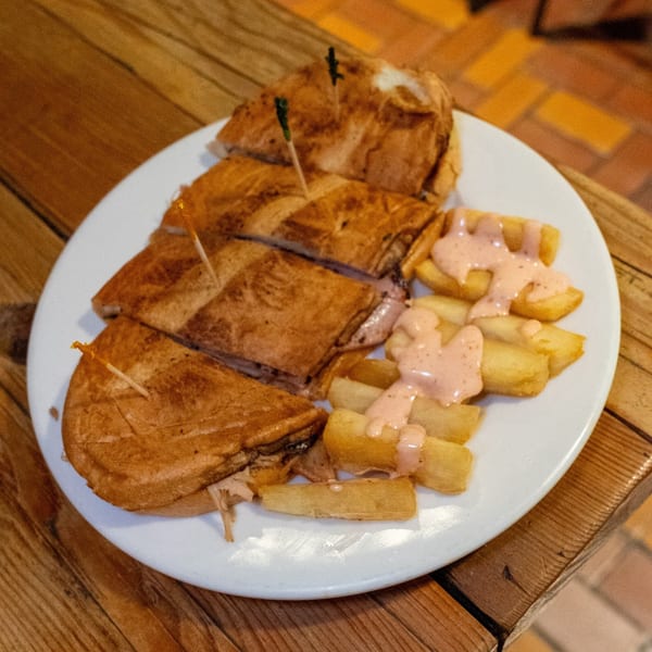 A Cuban sandwich, cut into triangles and held with toothpicks, served with yucca fries and pink sauce.