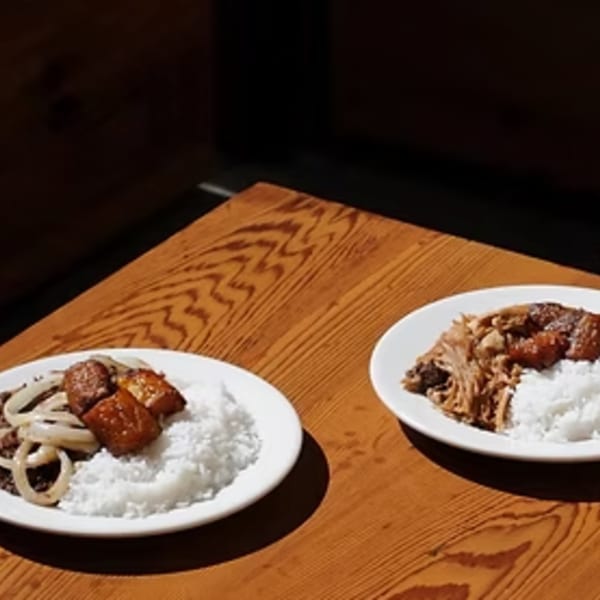 Two plates of Cuban food, one with meat and onions, the other with shredded pork and rice.