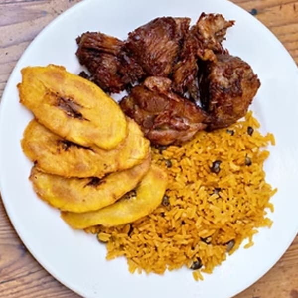 Cuban meal with fried plantains, dark meat, and yellow rice with black beans on a white plate.
