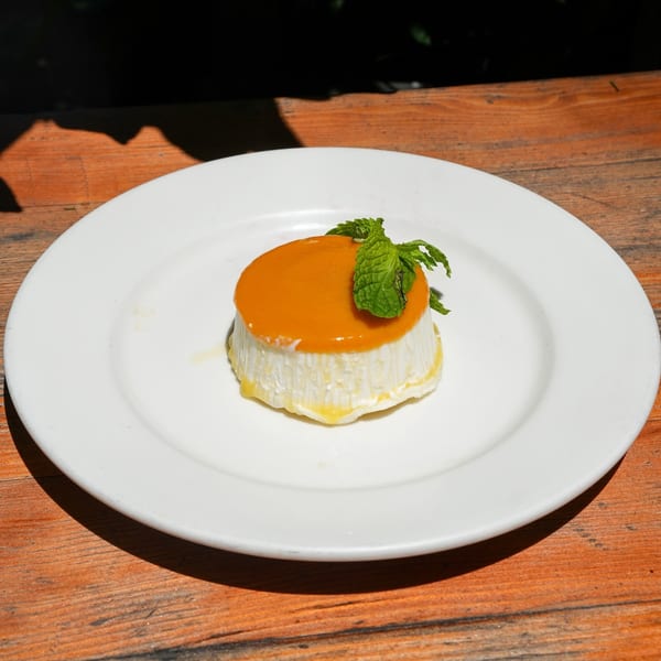 A white Cuban flan dessert with orange topping and mint garnish on a white plate.