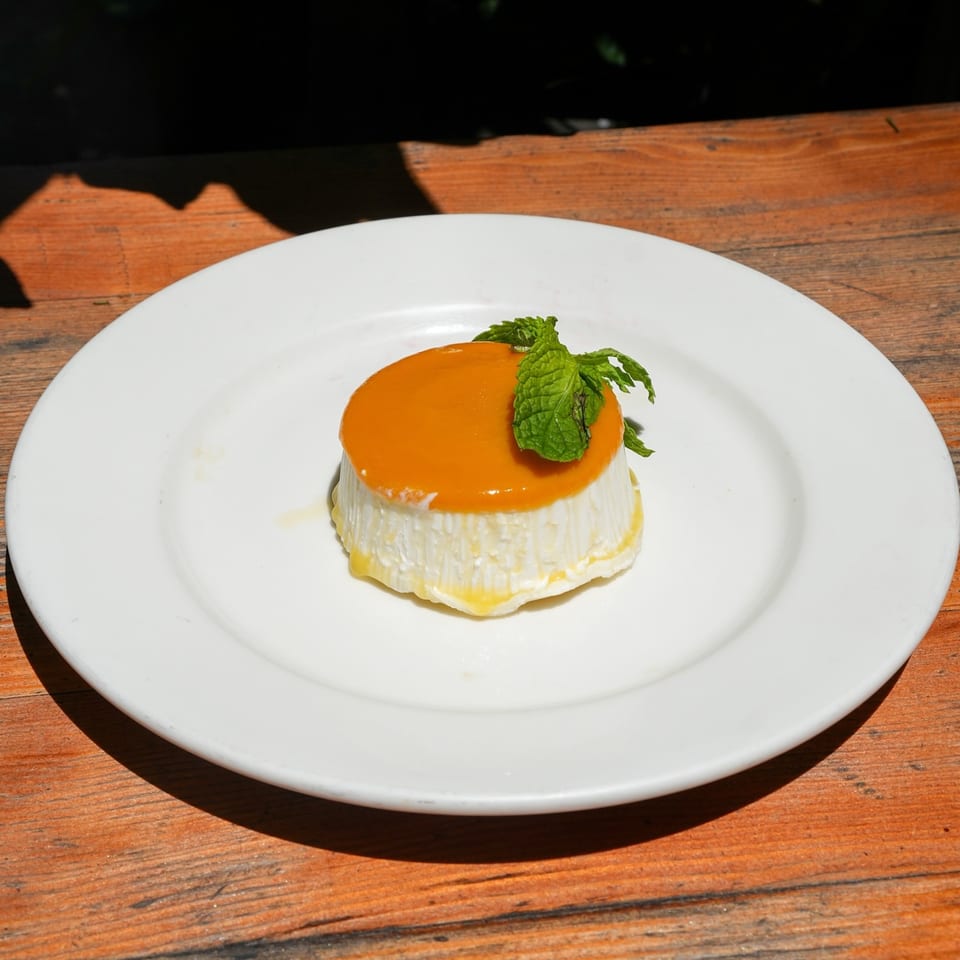 A white Cuban flan dessert with orange topping and mint garnish on a white plate.