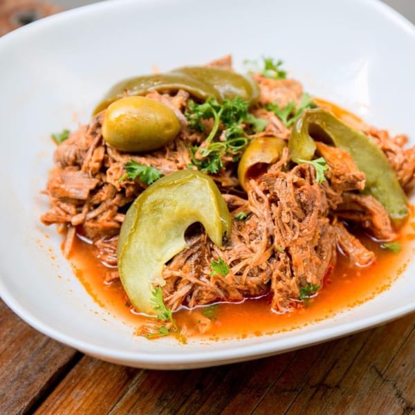 Close-up of a Cuban Ropa Vieja dish with shredded beef, green peppers, olives, and parsley.