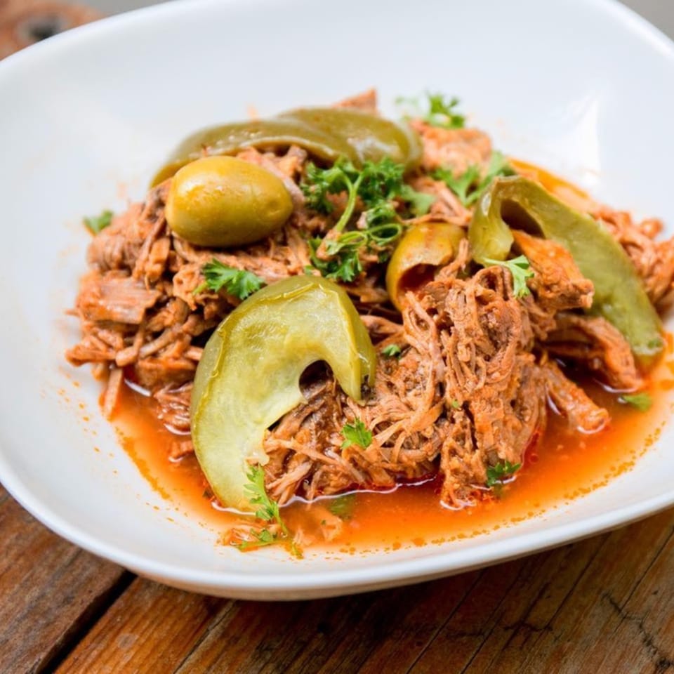 Close-up of a Cuban Ropa Vieja dish with shredded beef, green peppers, olives, and parsley.