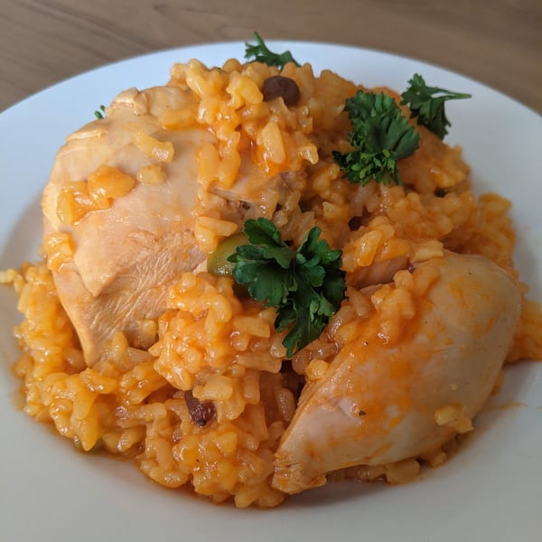 A close-up of Arroz con Pollo, a Cuban dish with chicken and yellow rice, garnished with parsley.