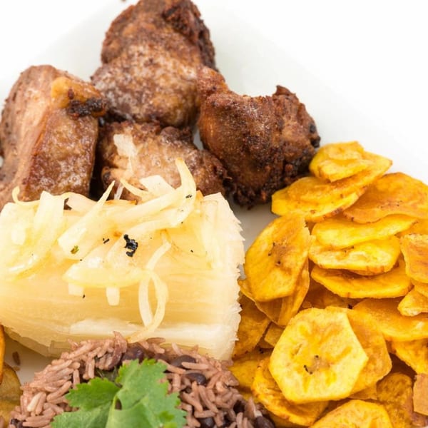Cuban dish with fried pork chunks, yuca with onions, plantain chips, and rice with beans.